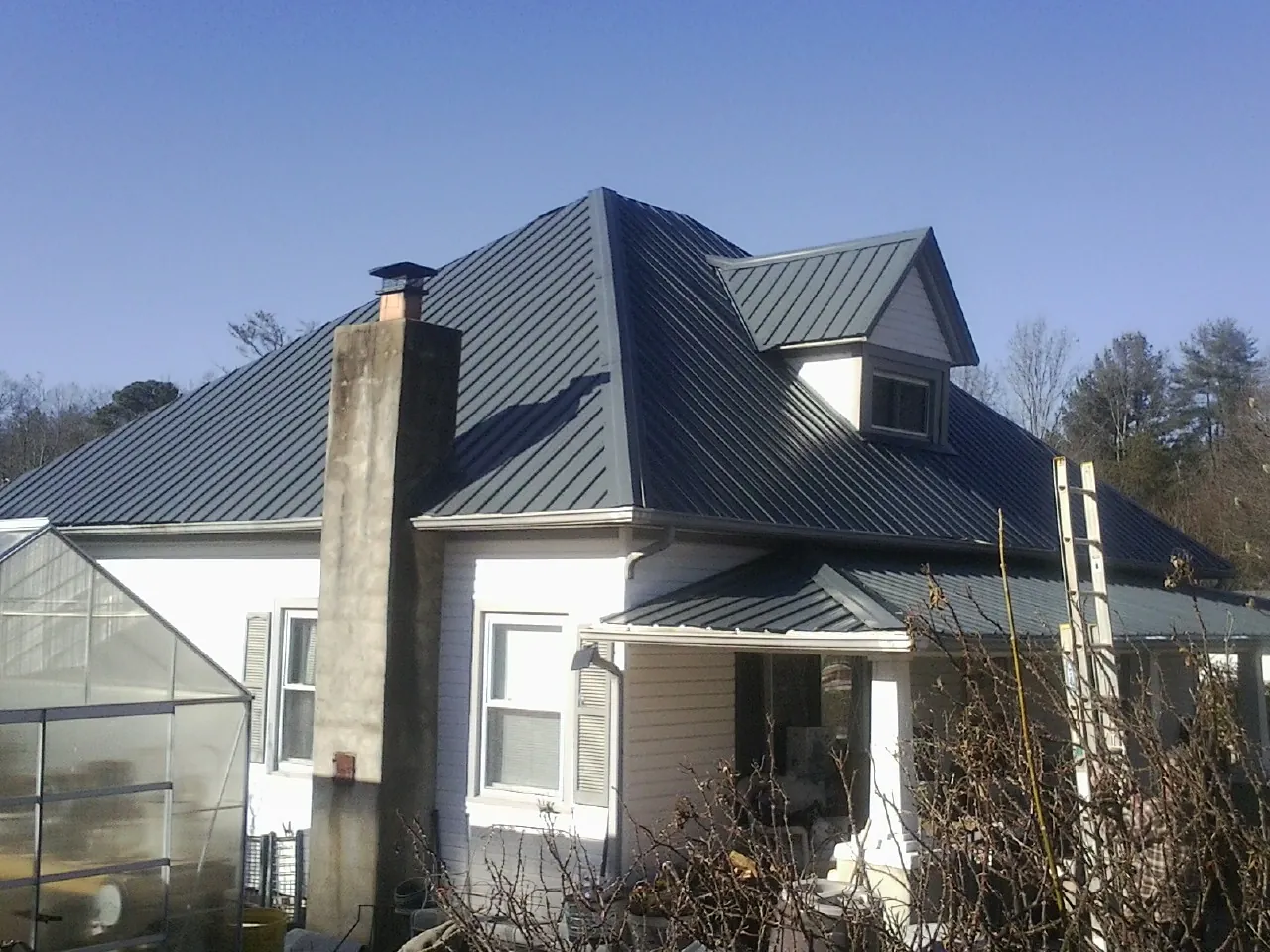 Dark blue standing seam metal roof on a white farmhouse with dormer — Slate & Tile Roof Repair by Roofing Brothers in Lawtell