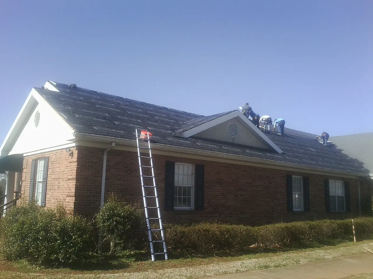 Crew tearing shingles off a brick ranch roof with a ladder set — Emergency Roof Repair work by our crew in Lawtell