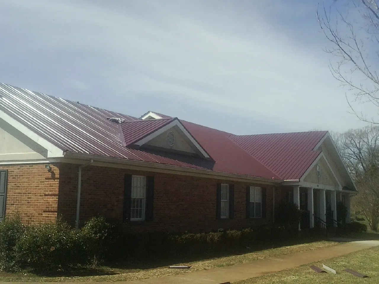 Red metal roof with gabled entries on a long brick building, from a Hail Damage Roof Repair job in Lawtell