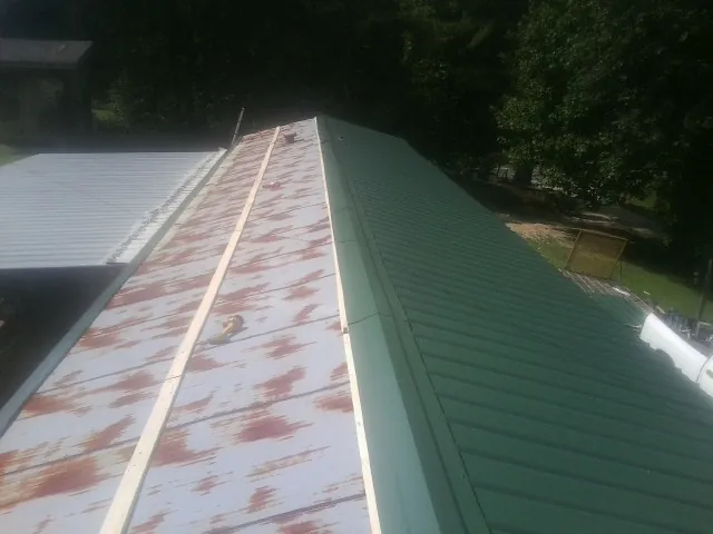 Old rusted panels beside newly installed green metal roofing — Wind Damage Roof Repair by Roofing Brothers in Lawtell