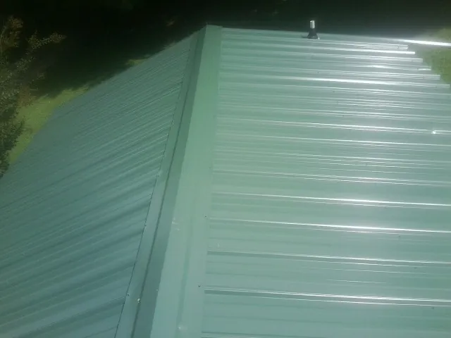 New green metal panels meeting at the ridge of a roof — Flat Roof Repair work by our crew in Lawtell