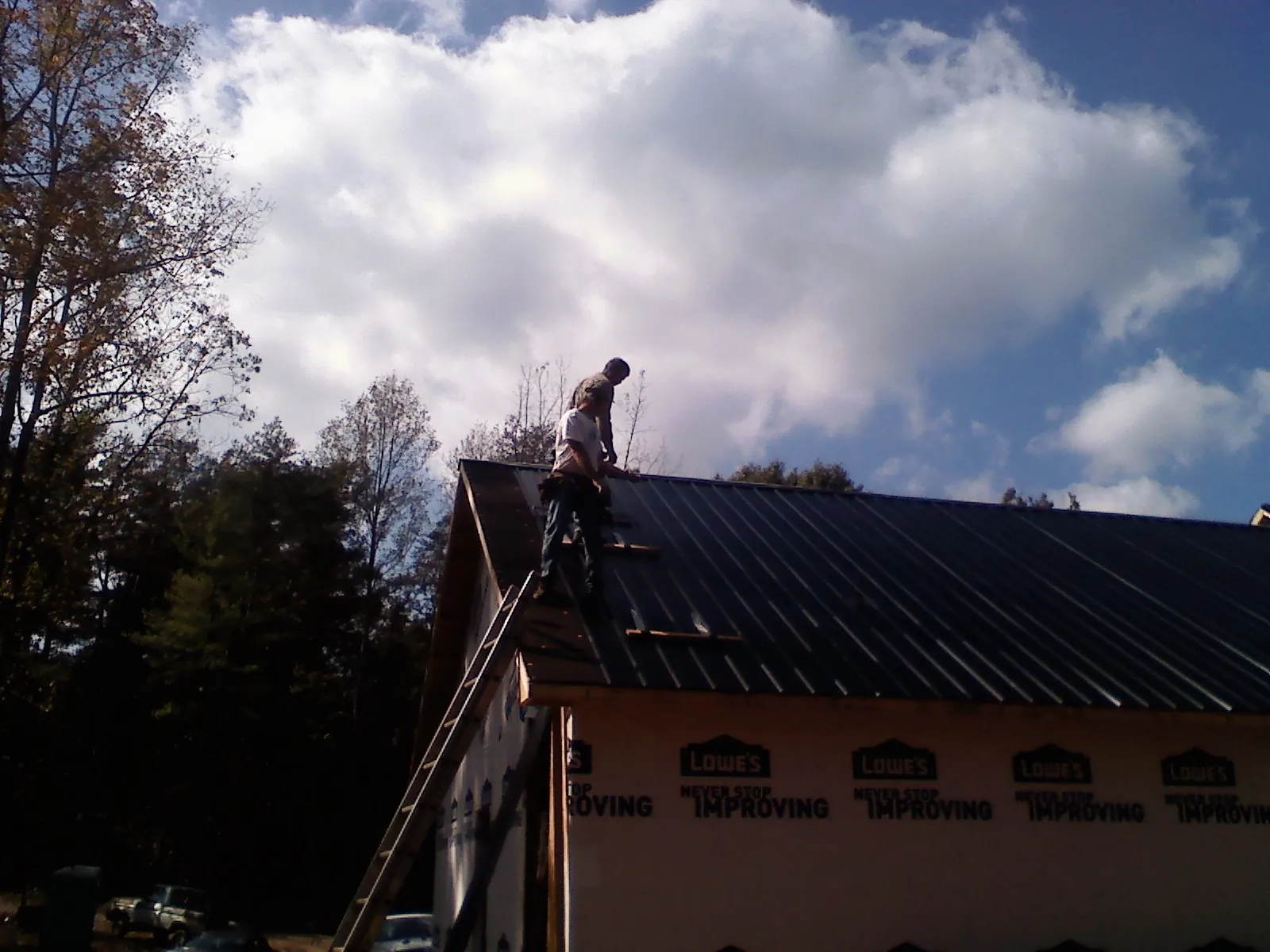 Roofer fastening dark metal panels high against a cloudy sky, from a Roof Inspection job in Lawtell
