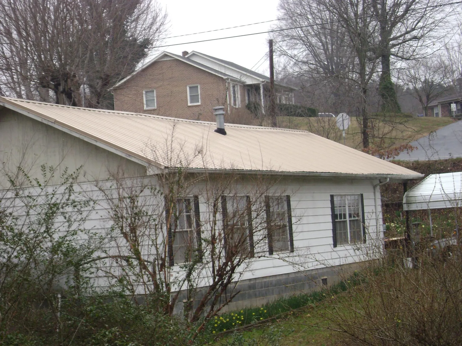 Tan metal roof on a white sided house set into a hillside — Commercial Roofing by Roofing Brothers in Lawtell