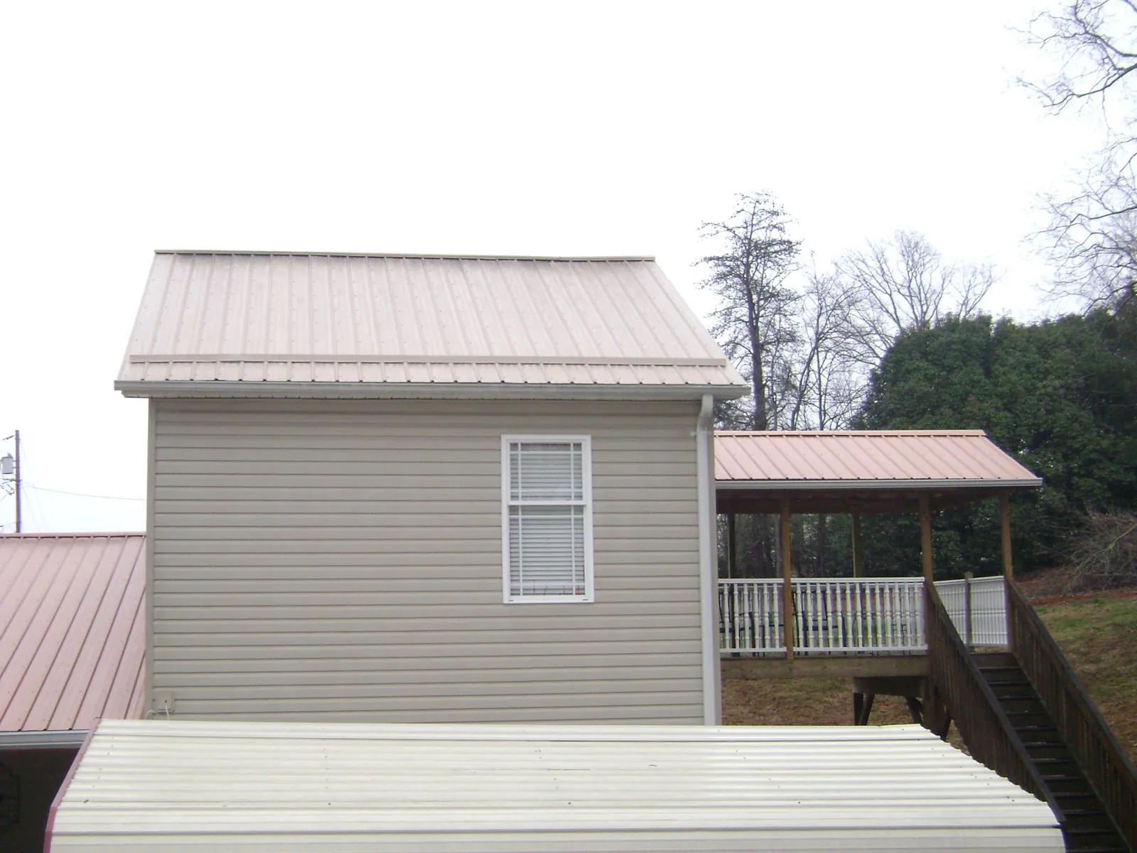 Tan metal roofs on a two story addition and attached porch, from a Roof Replacement job in Lawtell